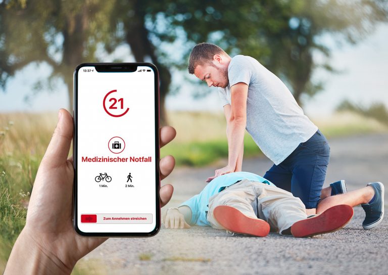Hand hält Handy mit Ersthelfer-App, im Hintergrund Reanimation